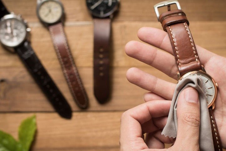 Somebody cleaning his watch over a table, where are displayed 3 other watches